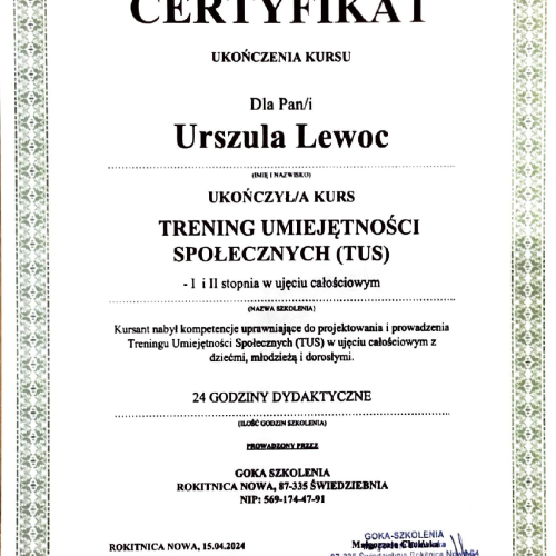 Szeroki widok na wnętrze fabryki samochodów. Na pierwszym planie widoczne są pomarańczowe barierki i element sterujący, a w tle pracownik w ciemnym kombinezonie wchodzi po schodach w kierunku nieukończonej karoserii samochodu na linii montażowej.